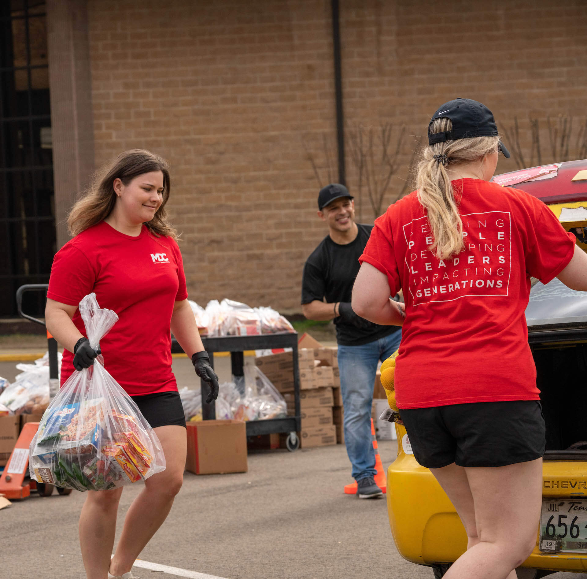 3 volunteers outside distributing food to yellow car